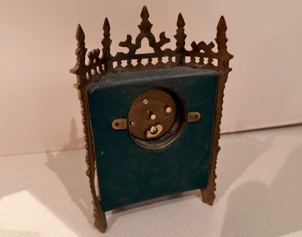 An ornate Victorian Gothic Revival gilt brass desk clock featuring pointed finials, twisted columns, and pleated pink silk side panels surrounding a central circular dial. View II