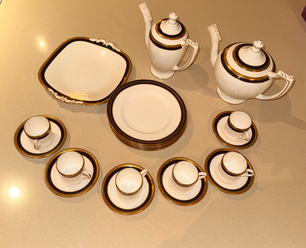 An antique white porcelain coffee service featuring cobalt blue borders and gold gilding, including a teapot, coffee pot, demitasse cups, saucers, side plates, and a serving dish.
