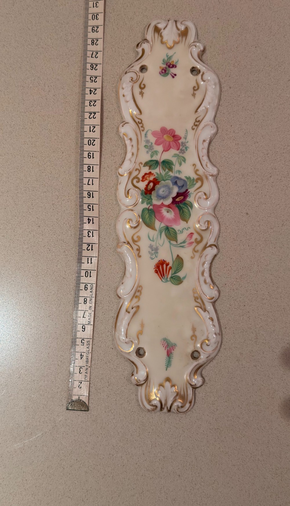 A Victorian porcelain door finger plate decorated with hand-painted floral motifs and gilded scroll edges.