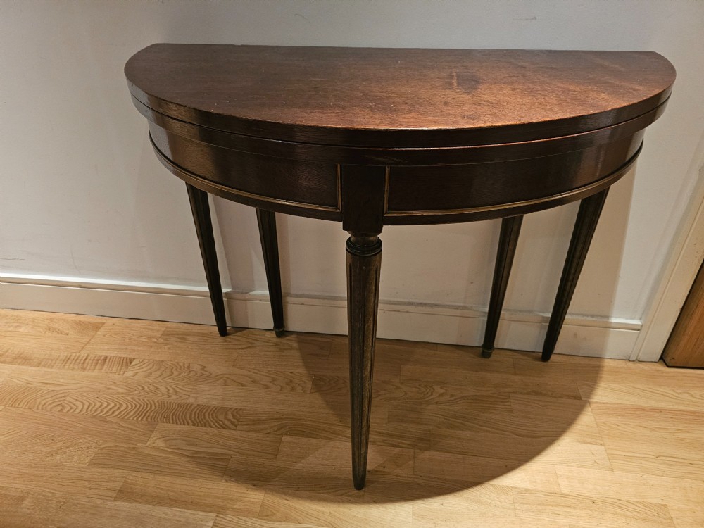 A 19th-century demilune dark mahogany console table featuring a hinged fold-over top and tapered fluted legs.
