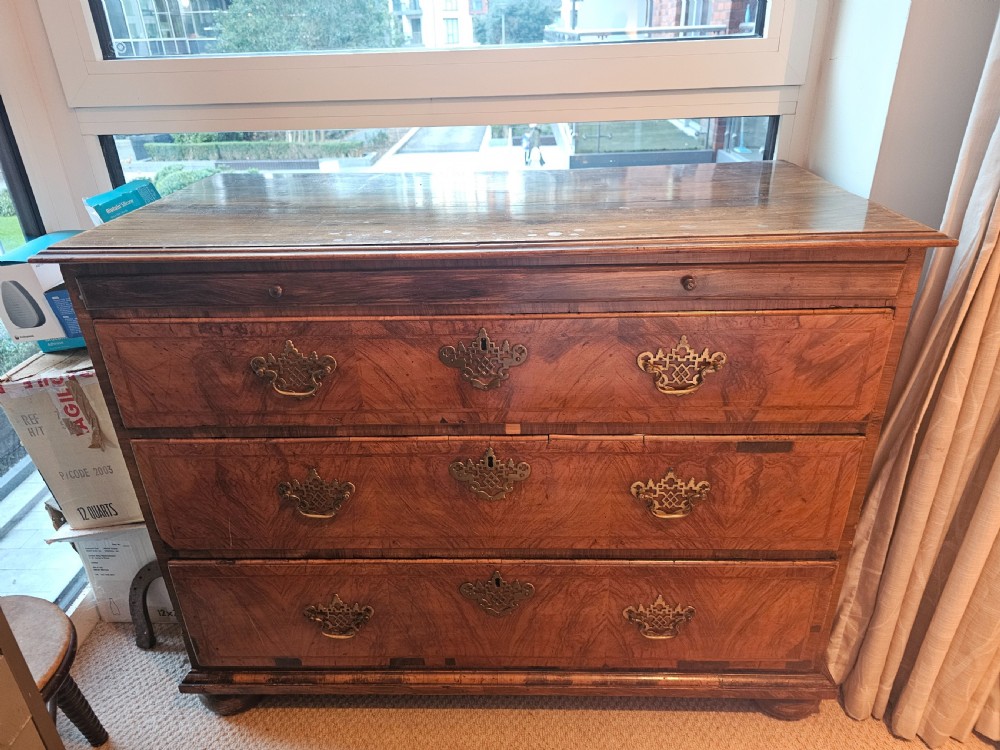 An 18th-century walnut chest of drawers featuring three crossbanded drawers, decorative pierced brass drop handles, keyhole escutcheons, and a sliding top panel.