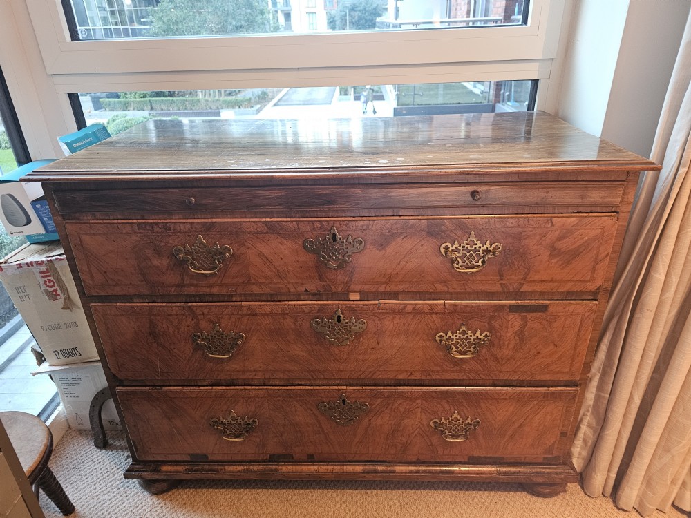 An 18th-century walnut chest of drawers with decorative brass handles and a sliding top panel.