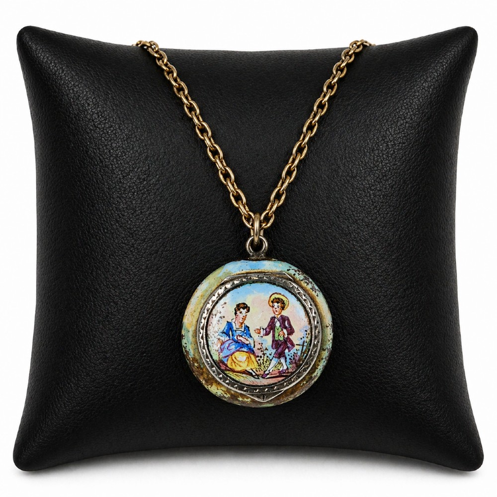 A circular double-sided enamel pendant necklace depicting a hand-painted scene of two figures in pastoral attire, set within a patterned silver border on a chain.
