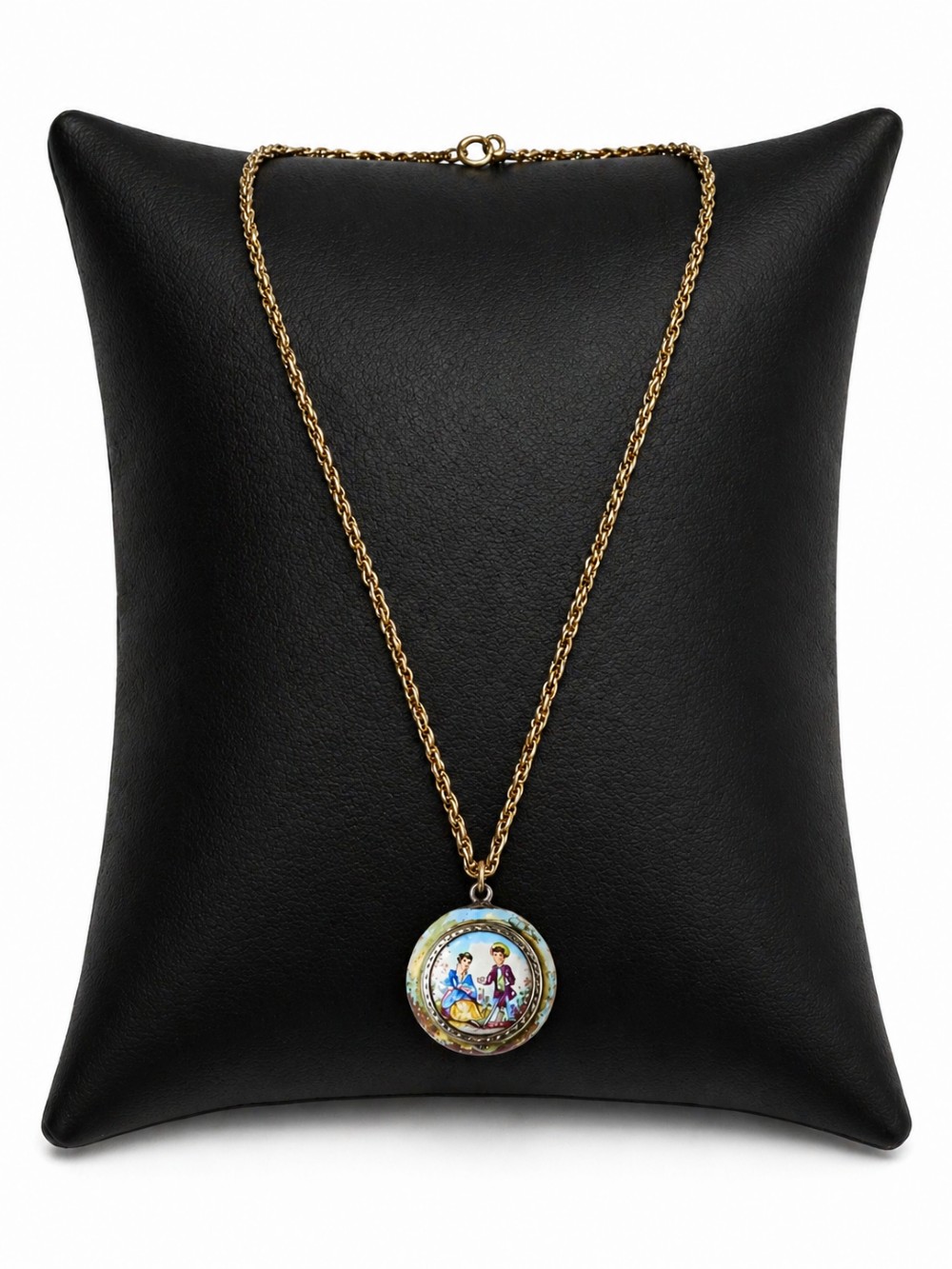 A circular double-sided enamel pendant necklace depicting a hand-painted scene of two figures in pastoral attire, set within a patterned silver border on a chain. View IV