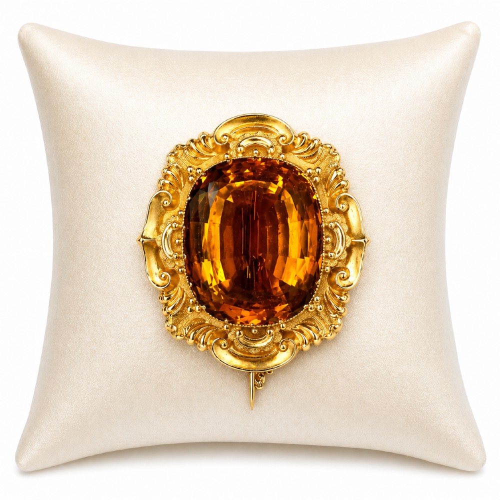 Victorian yellow gold brooch featuring a large oval faceted yellow topaz gemstone surrounded by an ornate scrollwork frame.