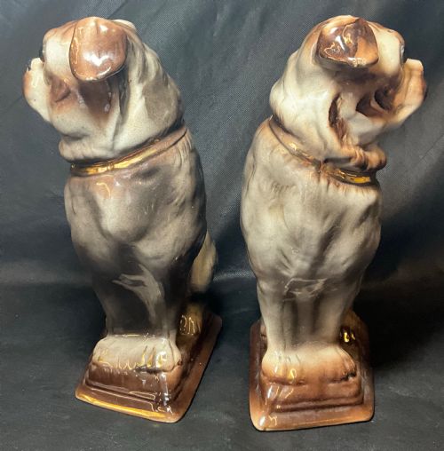 fig 1. A pair of facing Staffordshire earthenware pug dog figurines with brown glazed details and gilt collars seated on moulded octagonal bases.