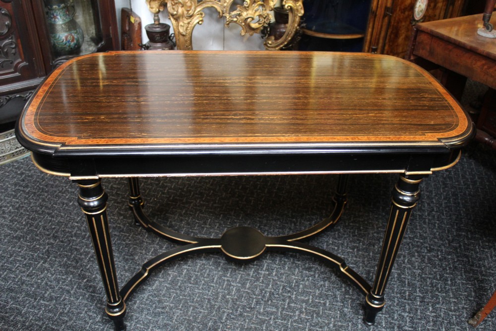 An antique ebonised side table featuring a patterned veneer top with crossbanded border, turned legs with gilt accents, and a curved X-form stretcher.