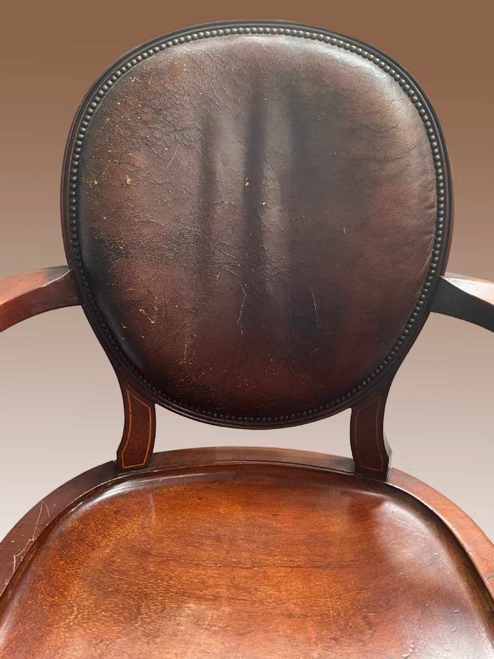 An English late nineteenth-century mahogany armchair featuring an upholstered dark leather oval backrest, curved armrests with inlay details, a shaped wooden seat, and cabriole legs. View II