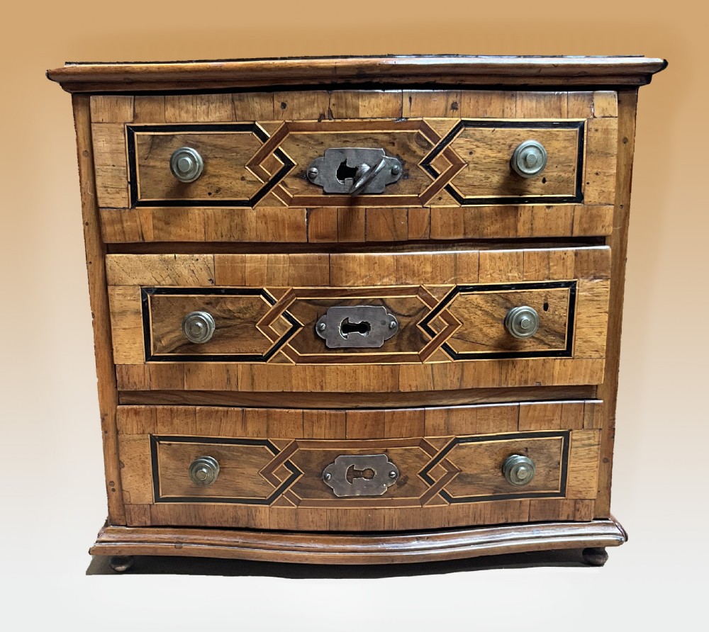 An early 19th century inlaid walnut serpentine fronted miniature chest of drawers