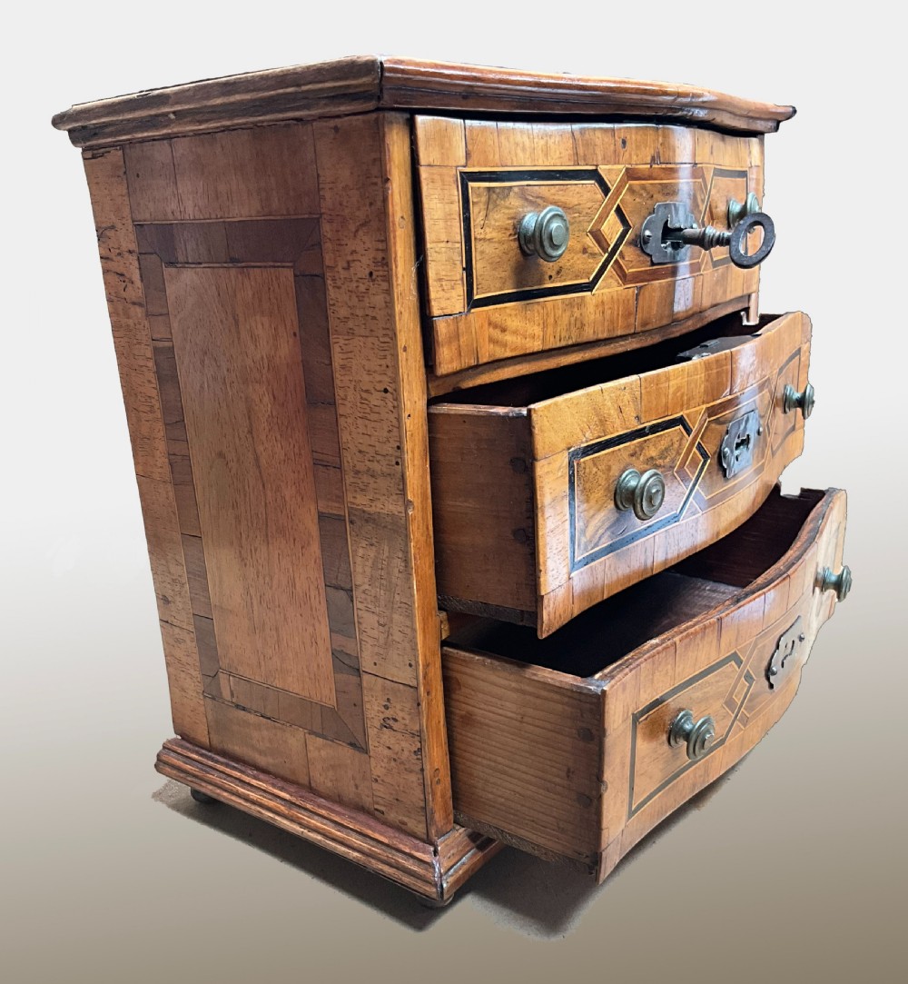 An early 19th century inlaid walnut serpentine fronted miniature chest of drawers View II