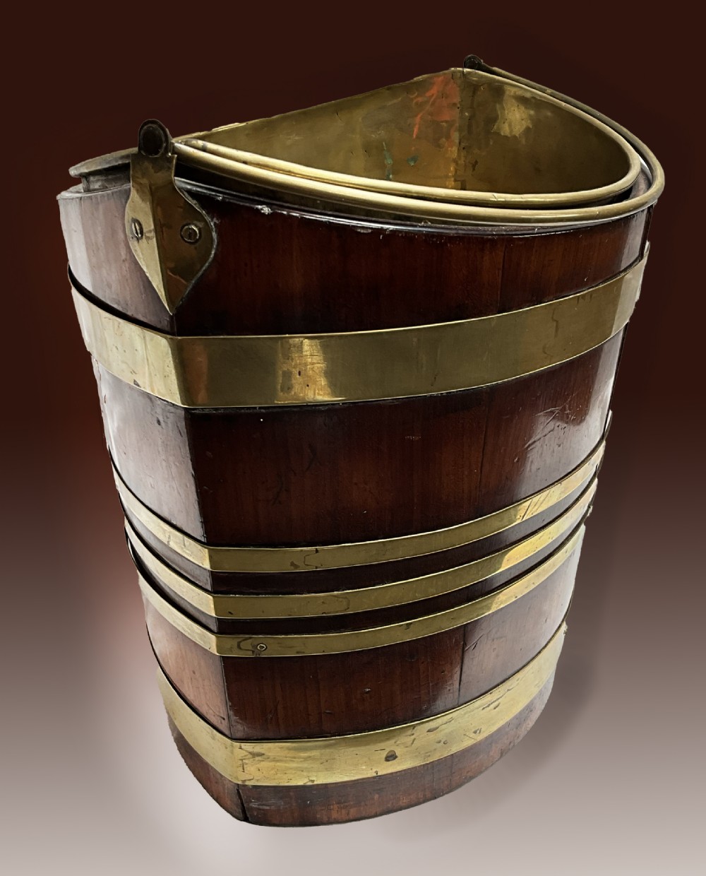 An early 19th-century elliptical mahogany bucket featuring horizontal brass banding, a brass swing handle, and a removable internal brass liner. View II