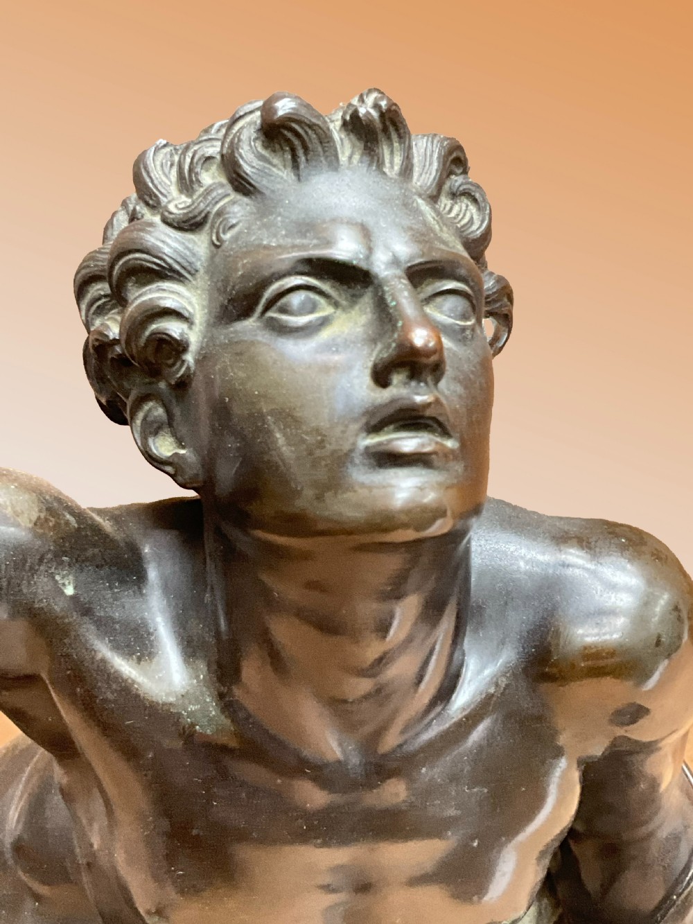 A patinated bronze sculpture depicting a semi-nude Classical soldier reclining on a rocky base with one arm raised aloft. View II