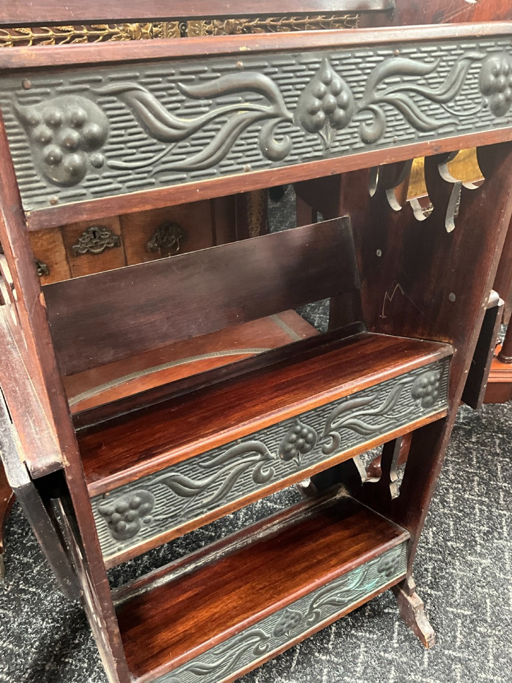 An Art Nouveau dark wood open bookcase featuring side drop-leaf shelves and decorative embossed metal panels with organic motifs. View VI