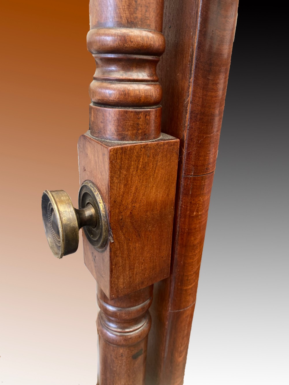 A Regency mahogany cheval mirror featuring a rectangular tilting glass frame supported by turned upright posts with finials, resting on reeded downswept legs with brass castors. View II