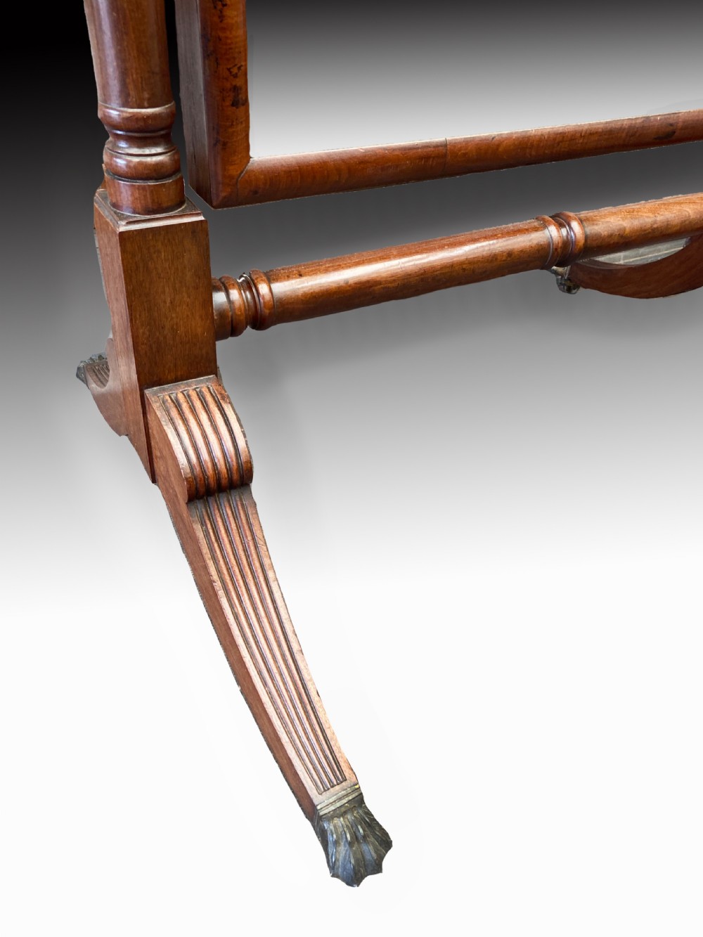 A Regency mahogany cheval mirror featuring a rectangular tilting glass frame supported by turned upright posts with finials, resting on reeded downswept legs with brass castors. View III