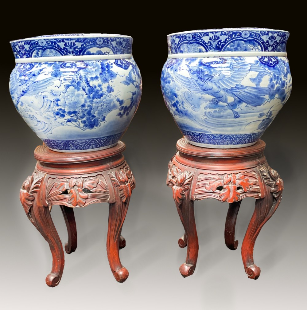 A pair of large round blue and white Japanese porcelain jardinieres decorated with avian motifs resting on intricately carved hardwood stands.