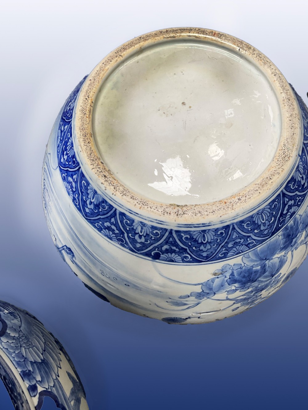 A pair of large round blue and white Japanese porcelain jardinieres decorated with avian motifs resting on intricately carved hardwood stands. View III
