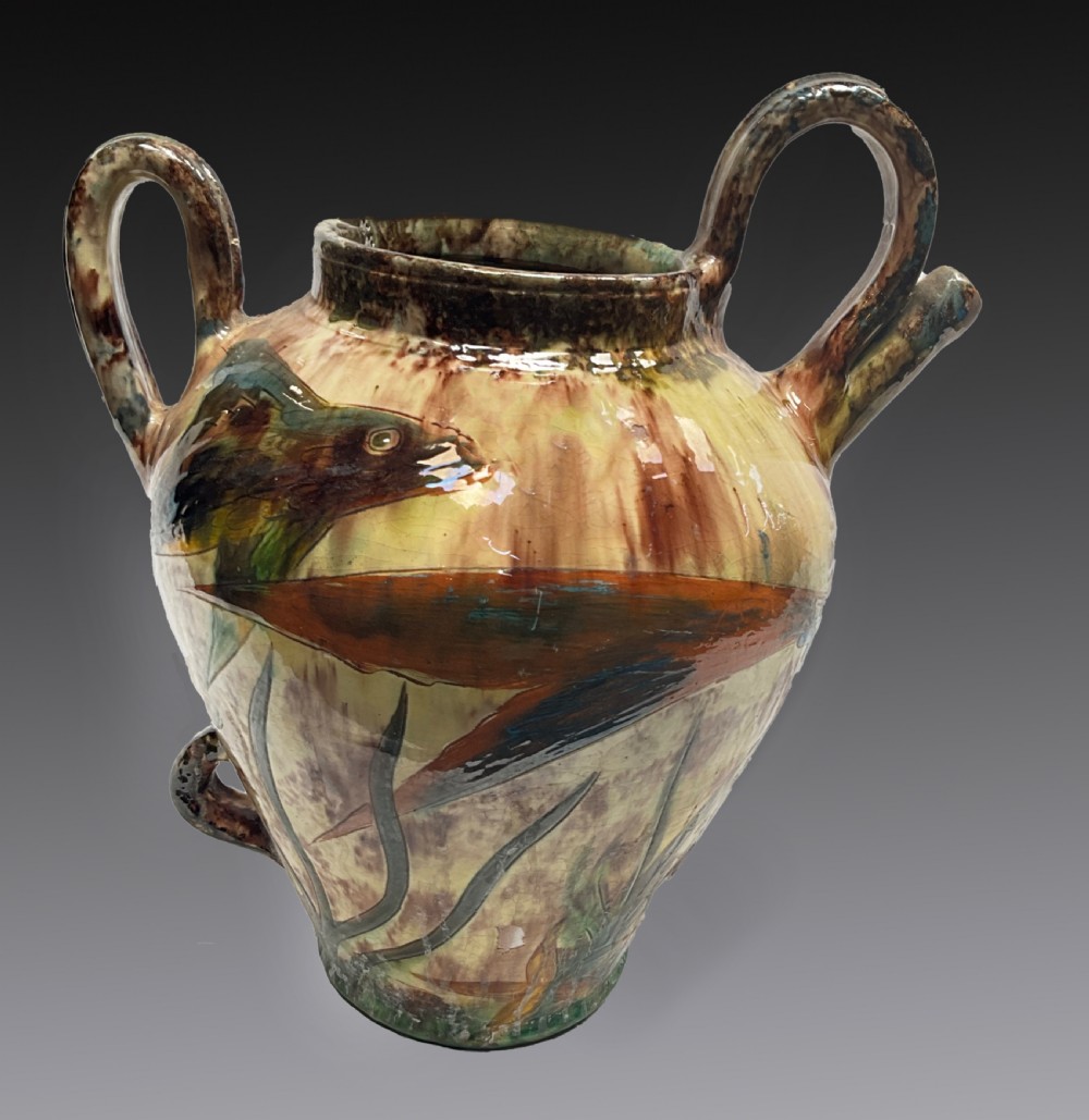 A glazed earthenware Devon pottery amphora decorated with painted fish motifs, featuring two upper handles and a variegated yellow, green, and brown finish.