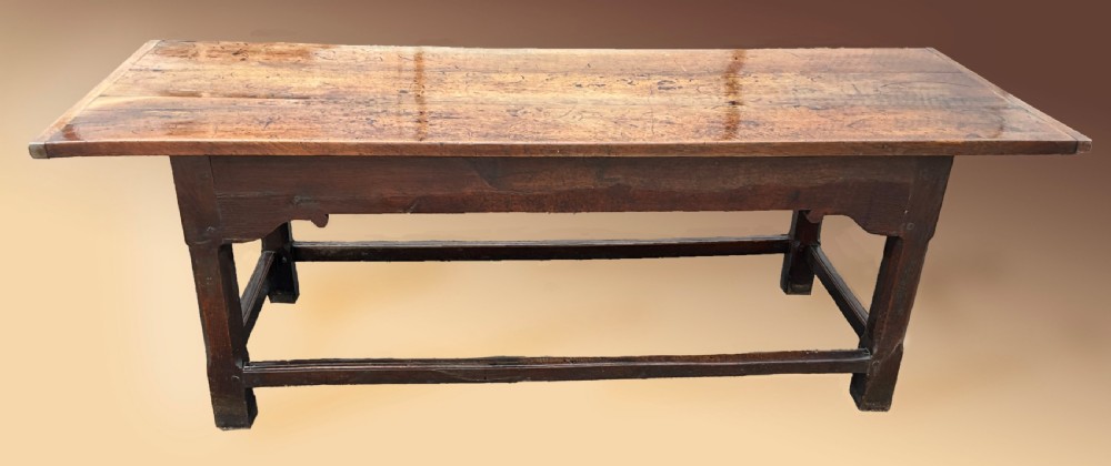 A long English oak refectory dining table featuring a three-plank top, breadboard ends, apron spandrels, and a low stretcher base.
