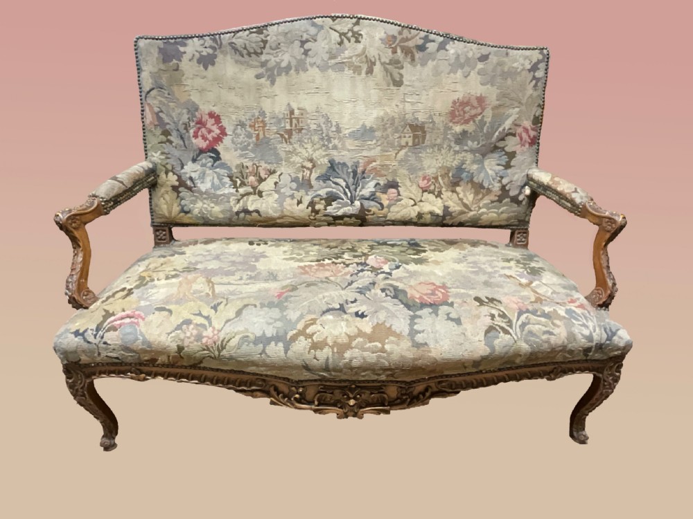 An 18th-century French carved wooden settee upholstered in a historic landscape and floral tapestry. View V