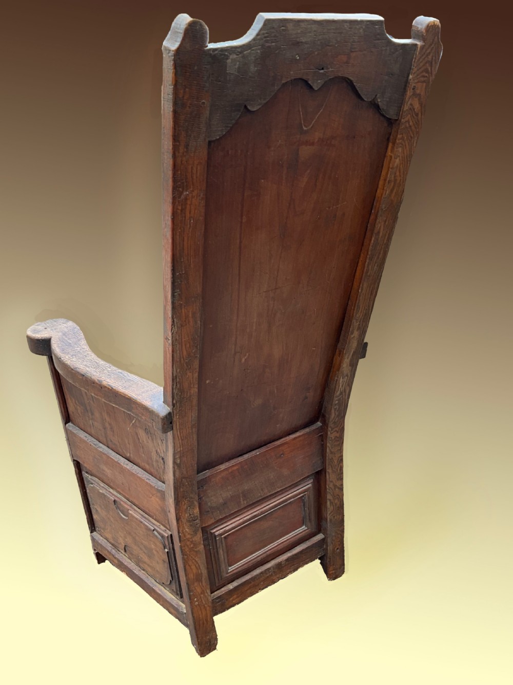 An antique dark oak Dutch country lambing chair featuring a high panelled back, broad flat armrests, and carved vertical accents. View II