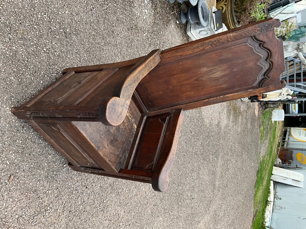 An antique dark oak Dutch country lambing chair featuring a high panelled back, broad flat armrests, and carved vertical accents. View VII