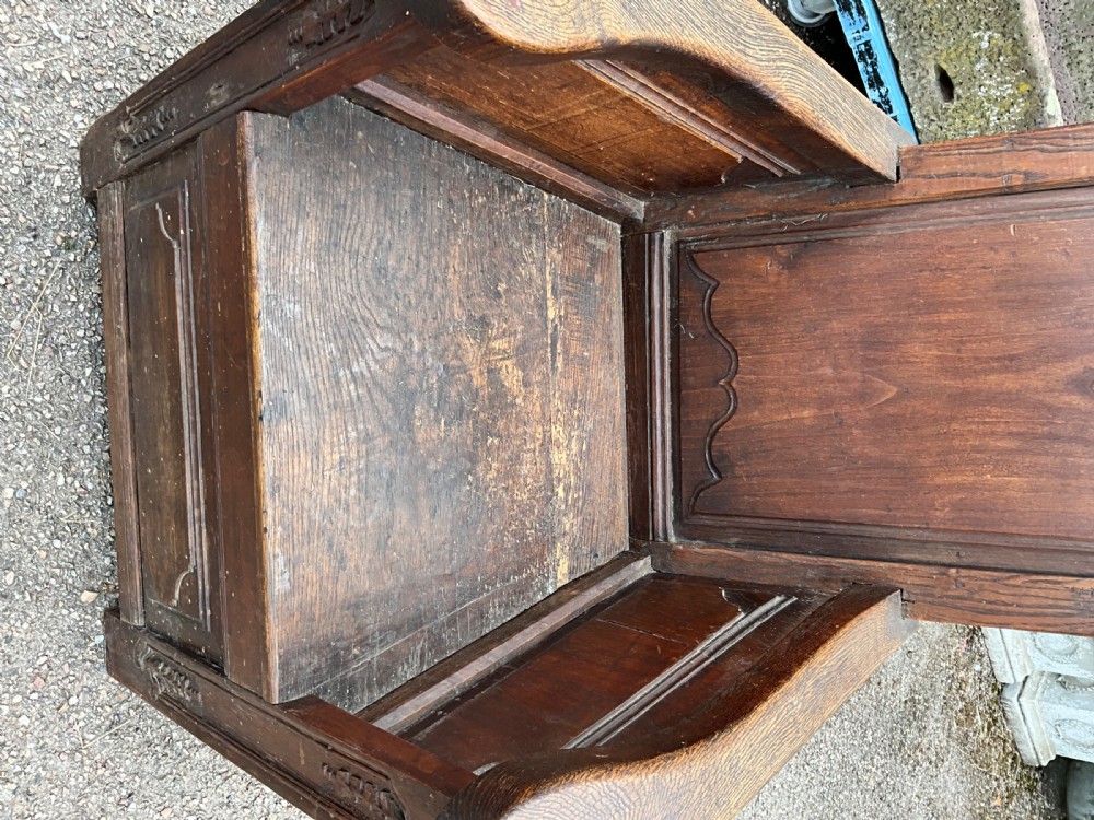 An antique dark oak Dutch country lambing chair featuring a high panelled back, broad flat armrests, and carved vertical accents. View VIII