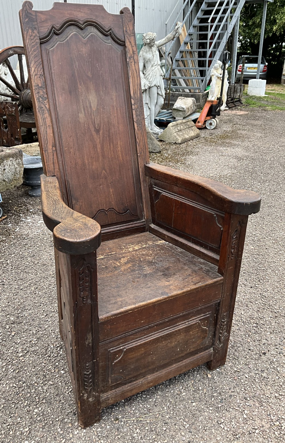 An antique dark oak Dutch country lambing chair featuring a high panelled back, broad flat armrests, and carved vertical accents. View XIII