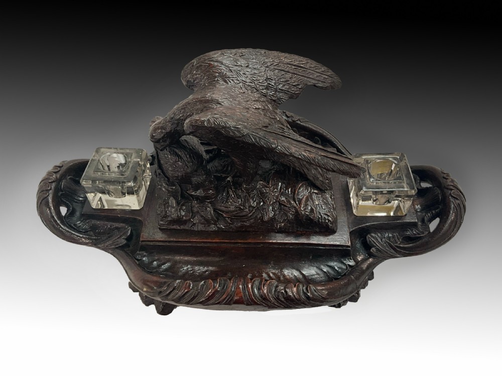 A carved dark wood Black Forest inkstand featuring a central eagle figure perched over prey, flanked by two square glass inkwells. View III