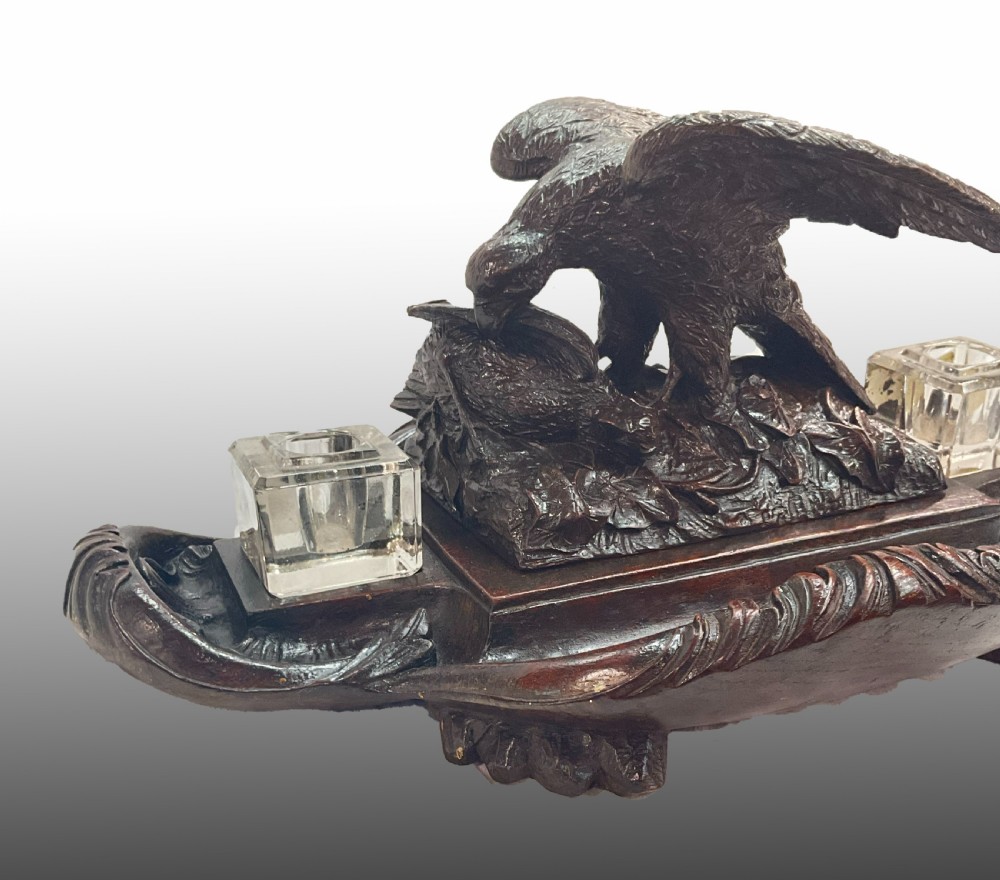 A carved dark wood Black Forest inkstand featuring a central eagle figure perched over prey, flanked by two square glass inkwells. View V