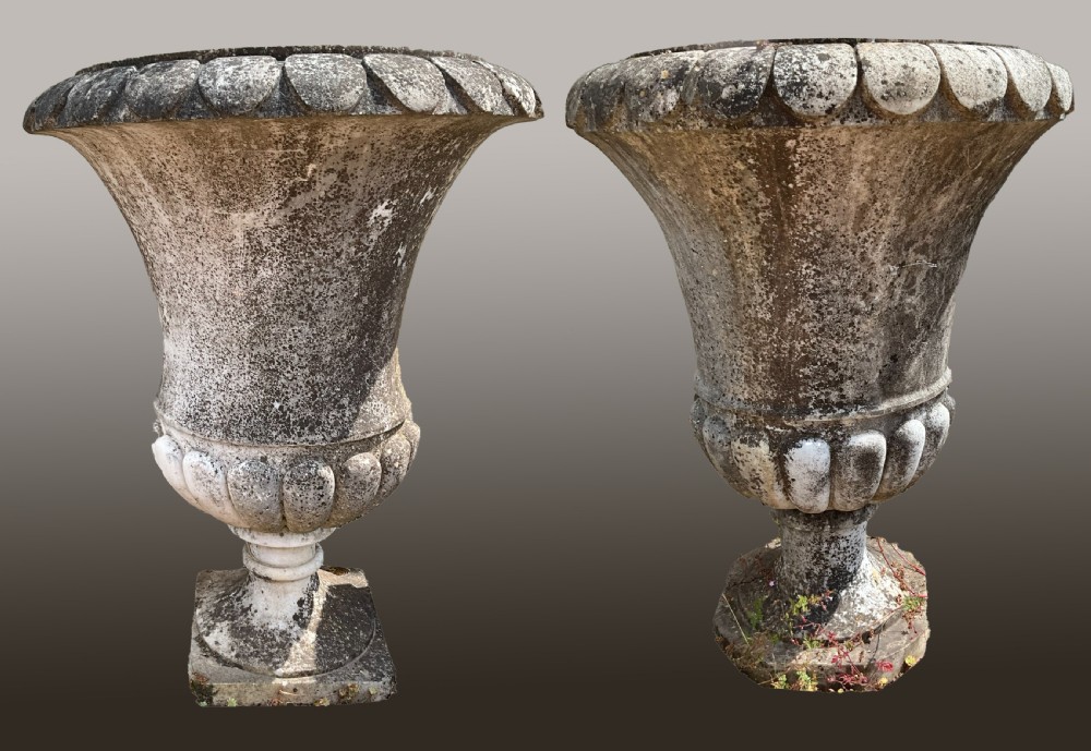 A near pair of large carved marble garden urns with weathered grey surfaces, gadrooned rims, and lobed bases.