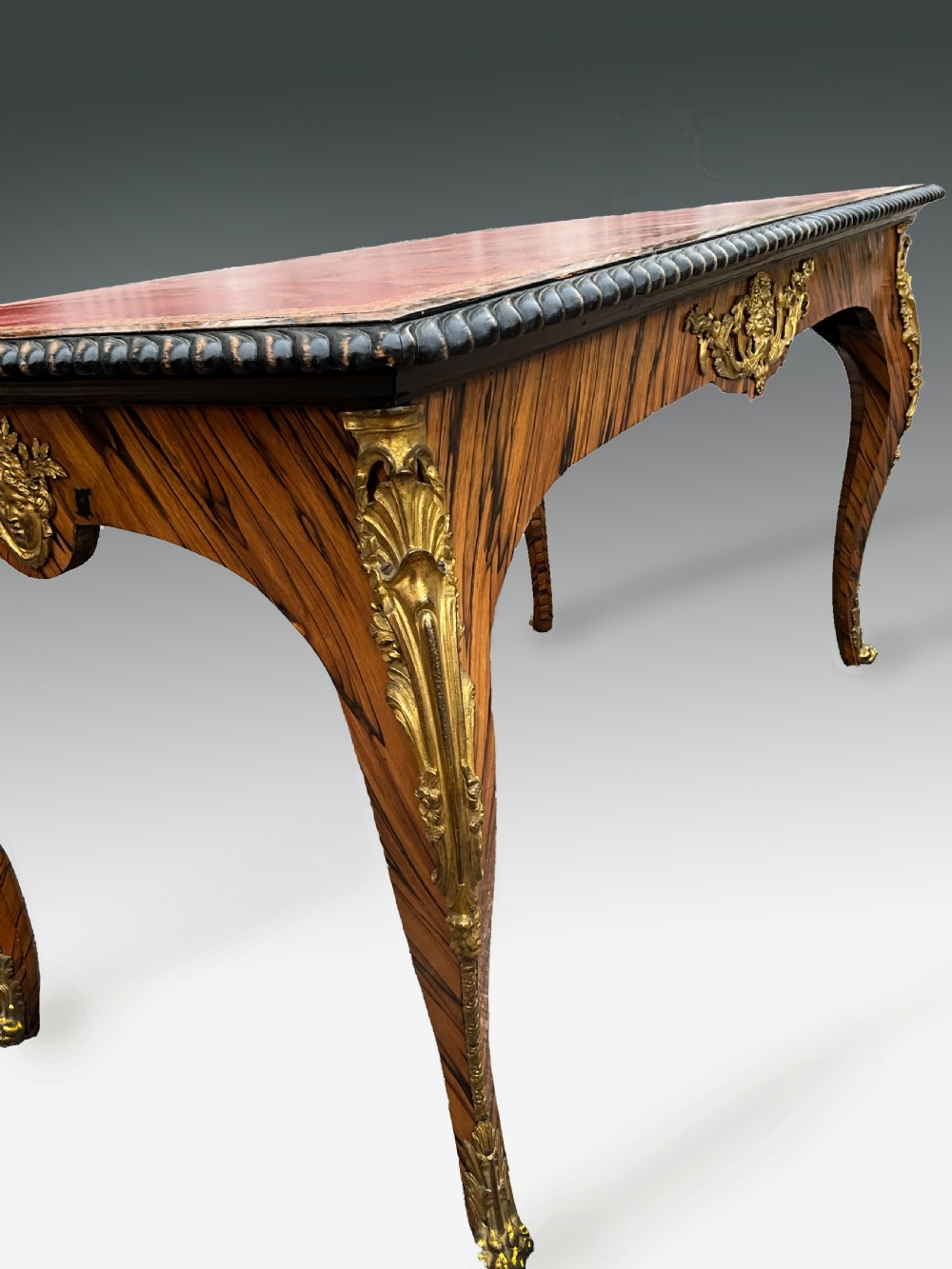 A French zebrawood writing table featuring a red leather top with gilt tooling, curved cabriole legs, and ornate gold-coloured mounts. View II