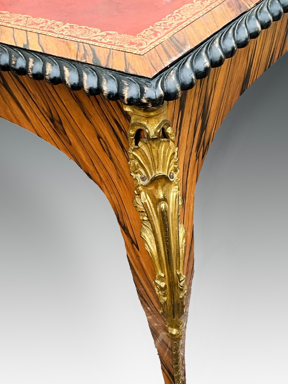 A French zebrawood writing table featuring a red leather top with gilt tooling, curved cabriole legs, and ornate gold-coloured mounts. View V