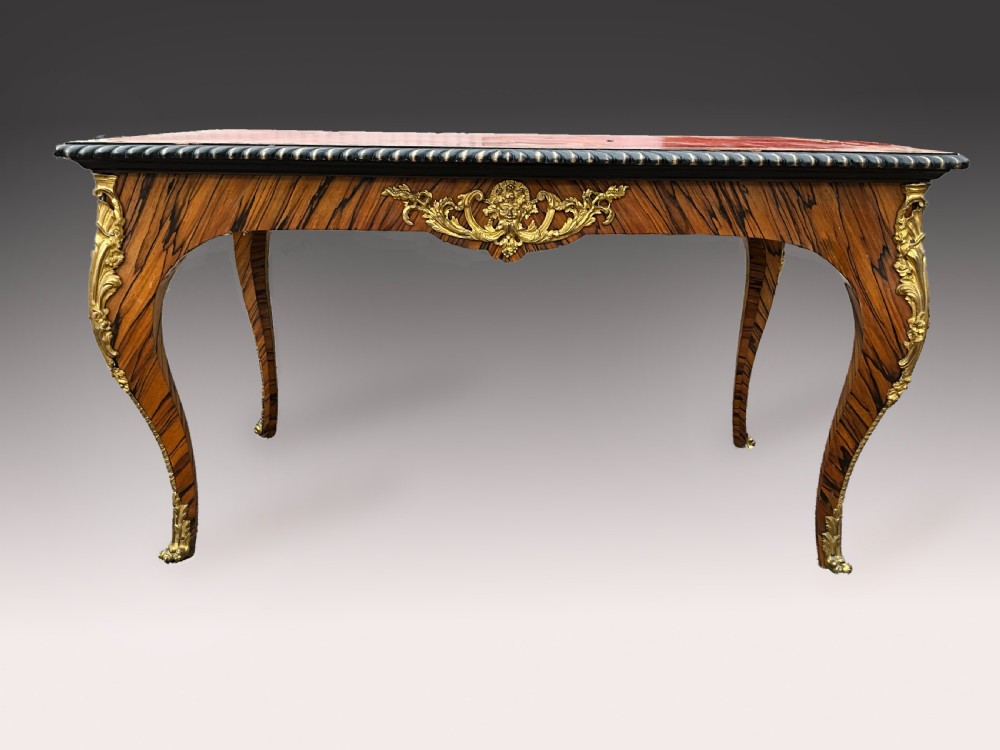 A French zebrawood writing table featuring a red leather top with gilt tooling, curved cabriole legs, and ornate gold-coloured mounts. View VI