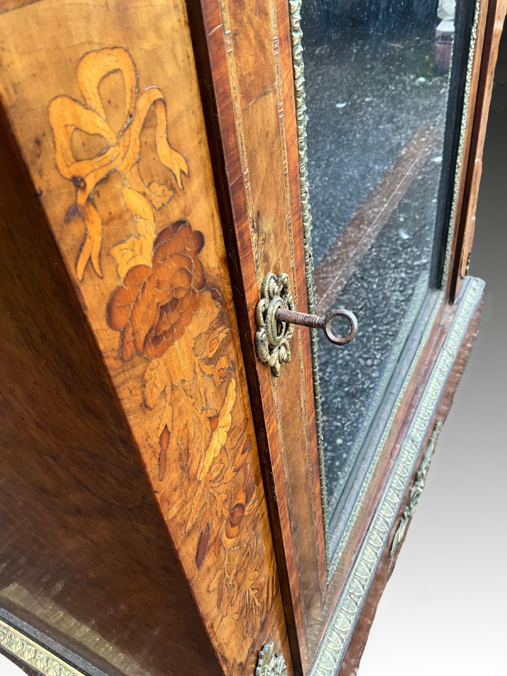 A Victorian burr walnut glazed cabinet featuring floral marquetry inlays, metal mounts, and a single glass door. View VII