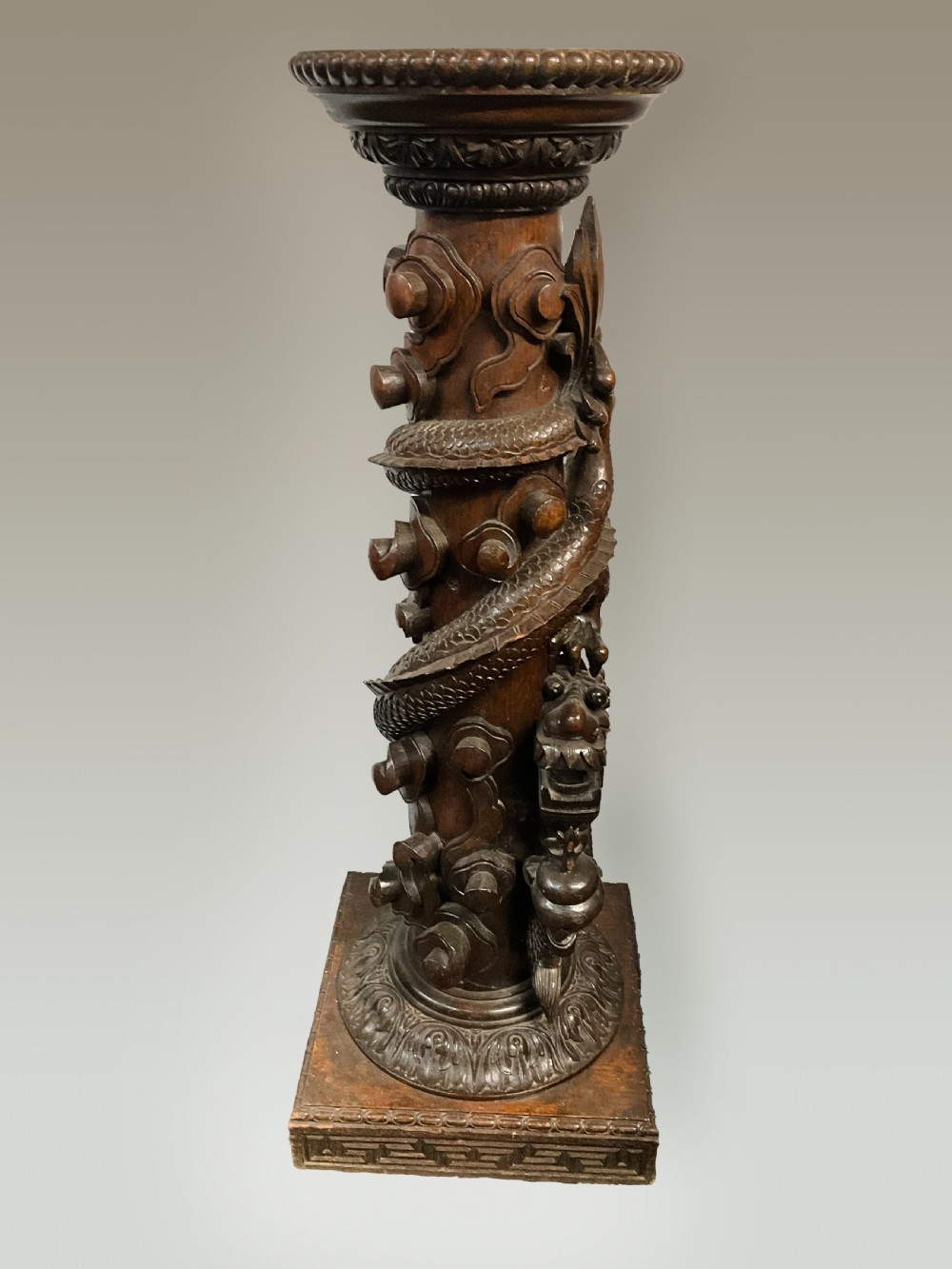 A tall dark brown hand-carved wooden column stand depicting a coiled dragon wrapped around the central shaft above a patterned square base.