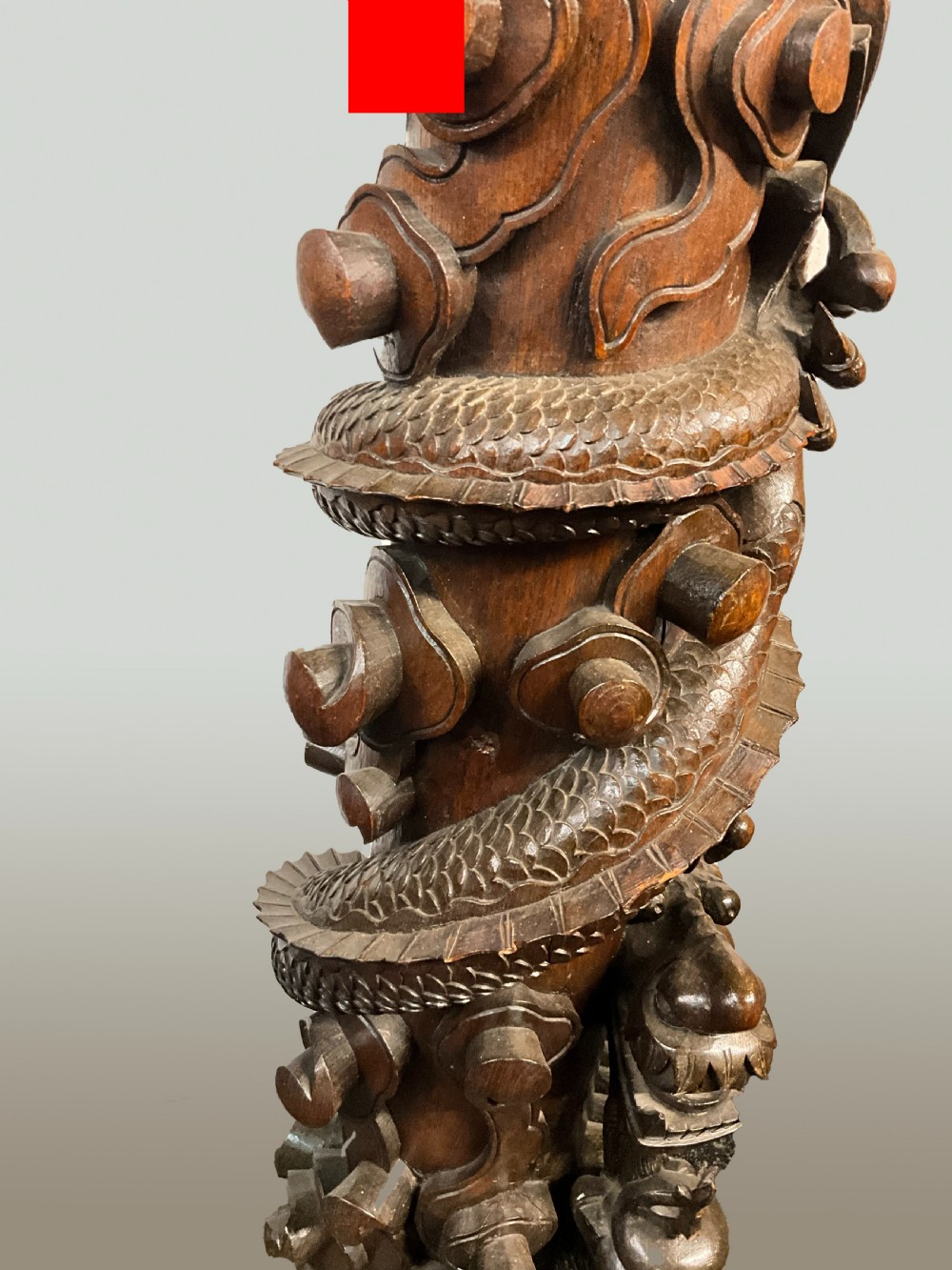 A tall dark brown hand-carved wooden column stand depicting a coiled dragon wrapped around the central shaft above a patterned square base. View VI