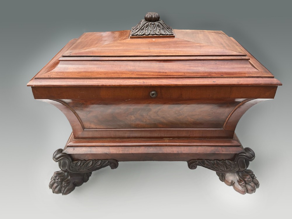 A Georgian mahogany sarcophagus wine cooler featuring a stepped lid with a carved acanthus finial and resting on four carved lion paw feet.