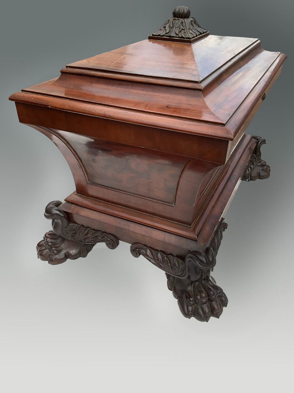 A Georgian mahogany sarcophagus wine cooler featuring a stepped lid with a carved acanthus finial and resting on four carved lion paw feet. View V
