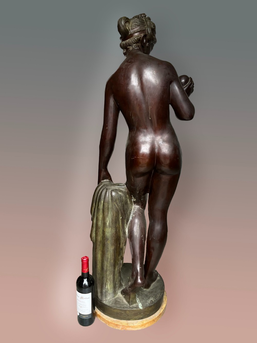 A classical bronze sculpture of a standing female figure holding a small sphere beside draped fabric on a marble base. View IV