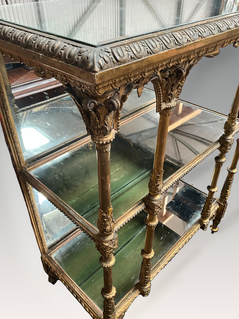 An ornate Victorian giltwood display shelf featuring three glass-tiered levels, a mirrored back panel, and intricate carved gesso columns with decorative moulding. View III