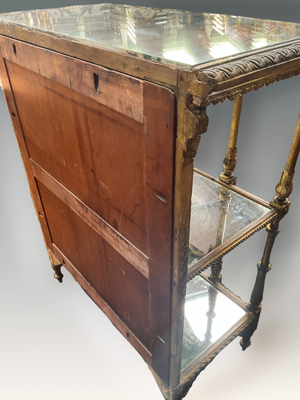 An ornate Victorian giltwood display shelf featuring three glass-tiered levels, a mirrored back panel, and intricate carved gesso columns with decorative moulding. View V
