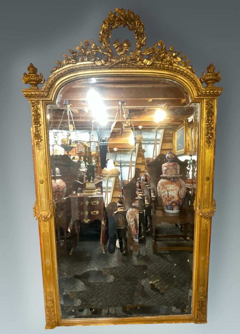 A large 19th-century French arched giltwood wall mirror with detailed wreath cresting and corner finials.