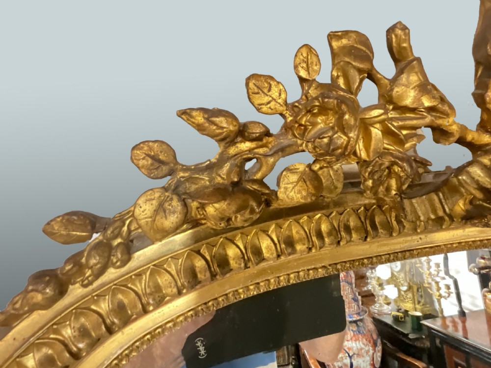 A large 19th-century French arched giltwood wall mirror with detailed wreath cresting and corner finials. View VI
