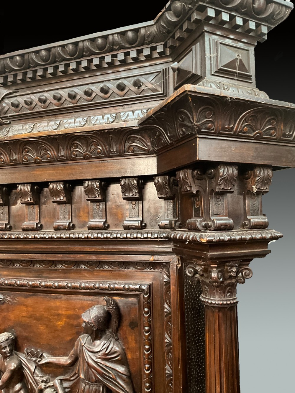 A tall dark walnut cabinet featuring detailed classical relief carvings on two door panels flanked by turned columns. View II