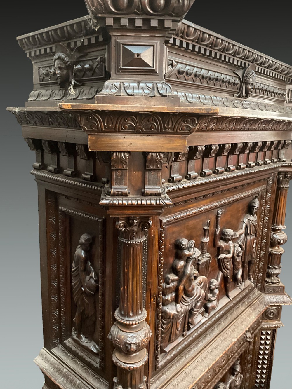 A tall dark walnut cabinet featuring detailed classical relief carvings on two door panels flanked by turned columns. View III