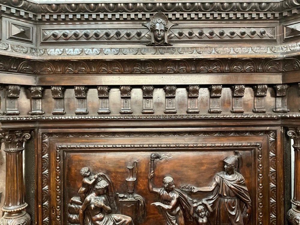 A tall dark walnut cabinet featuring detailed classical relief carvings on two door panels flanked by turned columns. View IV