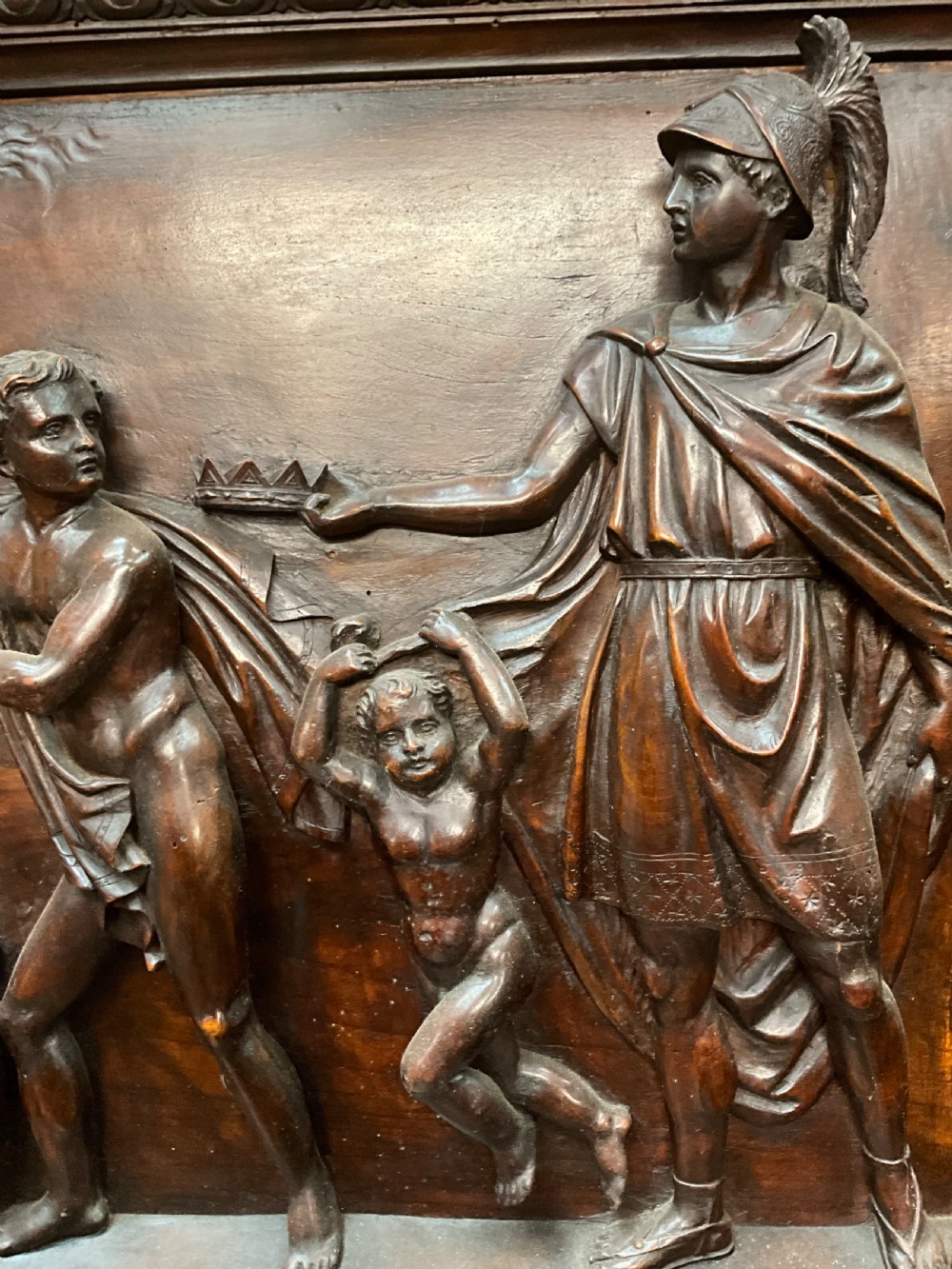 A tall dark walnut cabinet featuring detailed classical relief carvings on two door panels flanked by turned columns. View IX