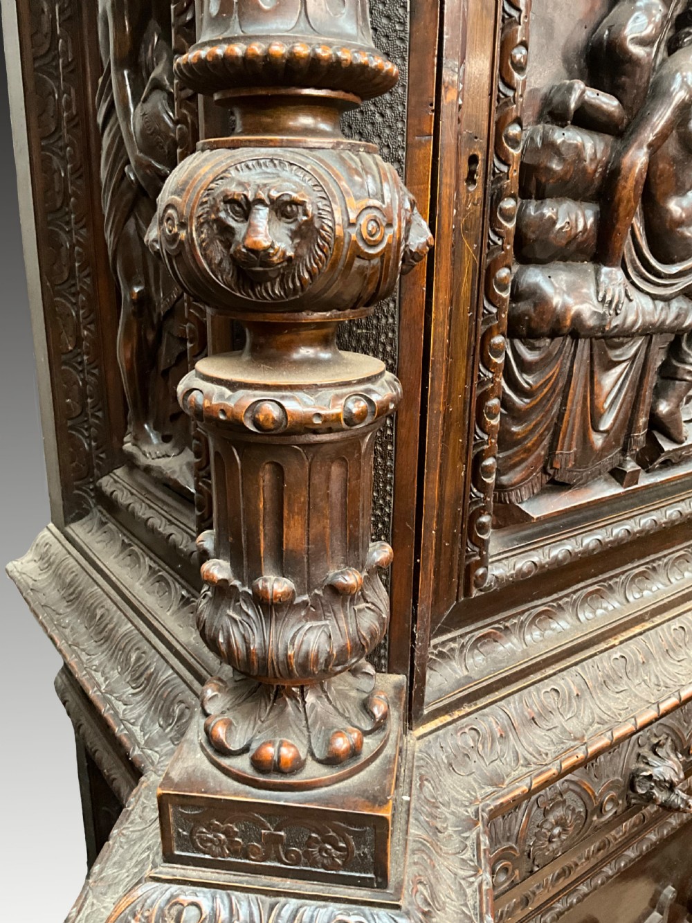 A tall dark walnut cabinet featuring detailed classical relief carvings on two door panels flanked by turned columns. View X