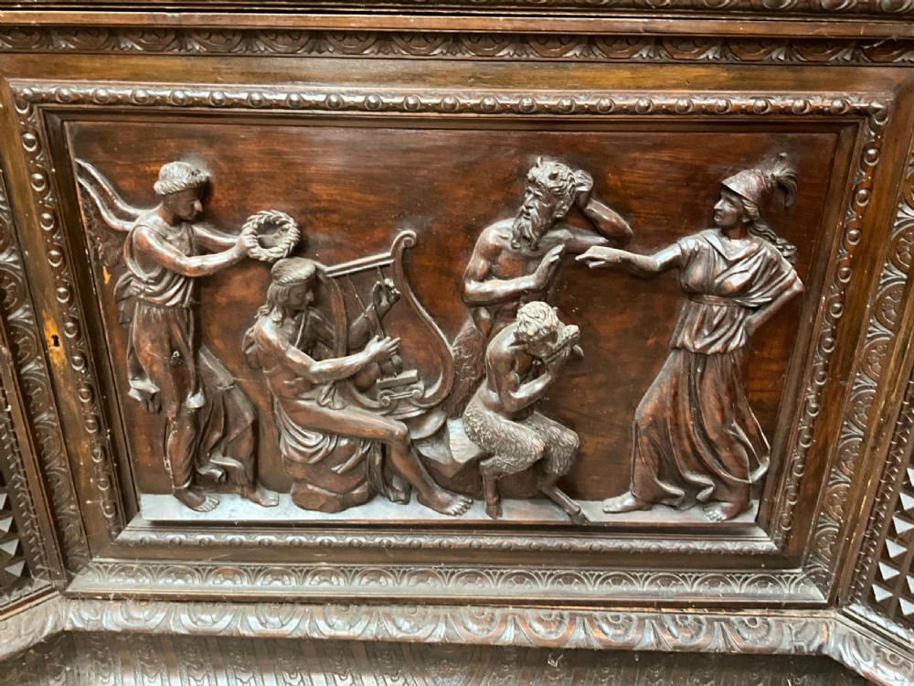 A tall dark walnut cabinet featuring detailed classical relief carvings on two door panels flanked by turned columns. View XI